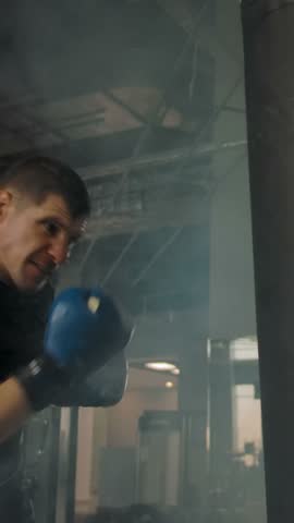 Side view of a young caucasian athlete wearing punching punching bag in a modern gym. Shooting in real time and in slow motion. Vertical shot.
