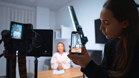 Professional camera and smartphone in girl's hand recording a female speaker. Women creating a blog content. - Powered by Shutterstock - Get 15% off with code: PIKWIZARD15