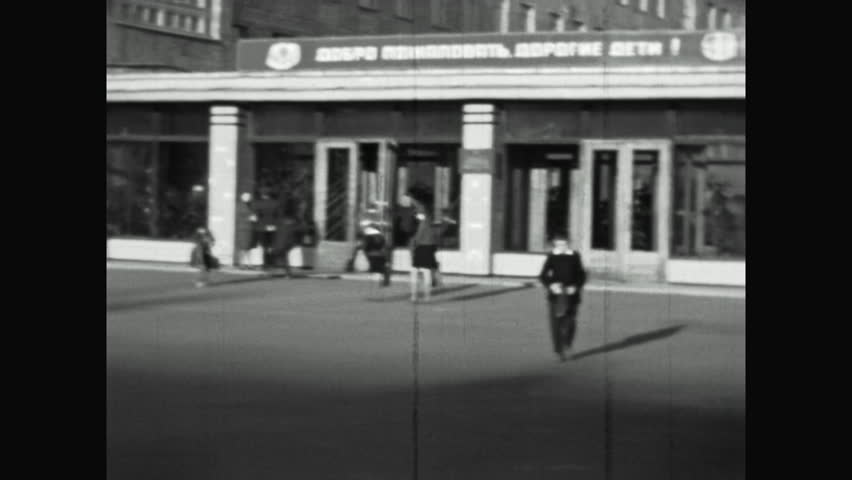 Retro film, School children go to elementary school on sunny morning, outdoors. students kids in School yard exterior. Schoolchildren walking into education institution building. Vintage archive 1960s