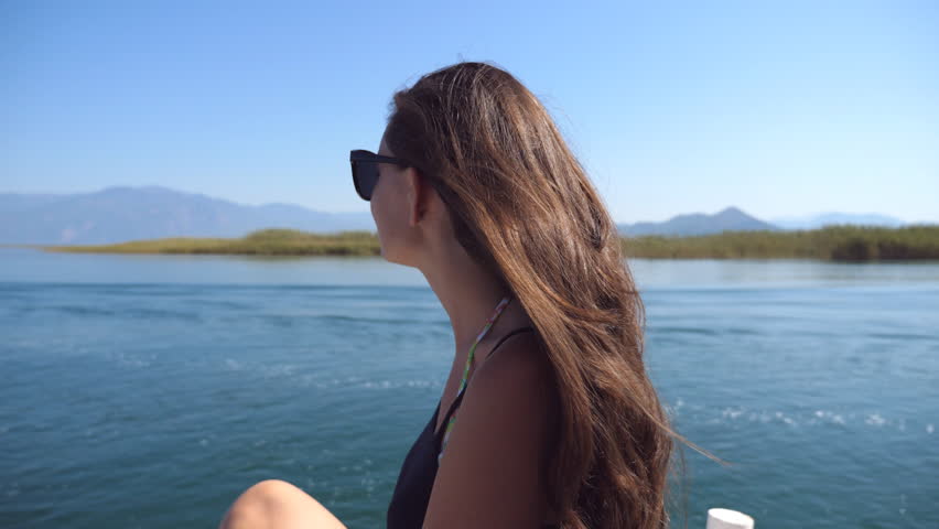 Profile of young girl sitting on bow of boat and looking to beautiful nature landscape during trip. Happy woman enjoying summer travel. Vacation or holiday concept. Close up Slow motion