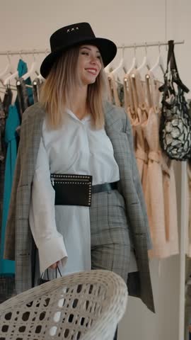 Low angle tracking shot of gorgeous excited women in stylish clothes looking away and smiling, while going out showroom of contemporary boutique in slow motion. Vertical shot.