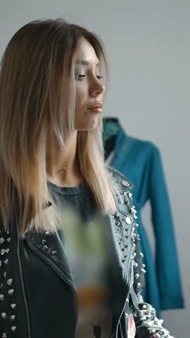 Young female in trendy outfit smiling and selecting new garment from clothes rail in slow motion while shopping in weekend. Vertical shot.