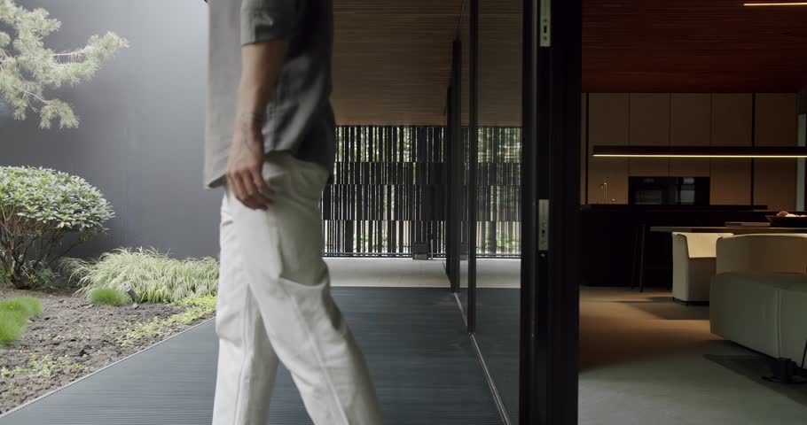 A stylish man steps into a sleek, contemporary home featuring minimalist design, a serene garden, and sophisticated interiors. Man Walking into a Modern Home with Minimalist Architecture