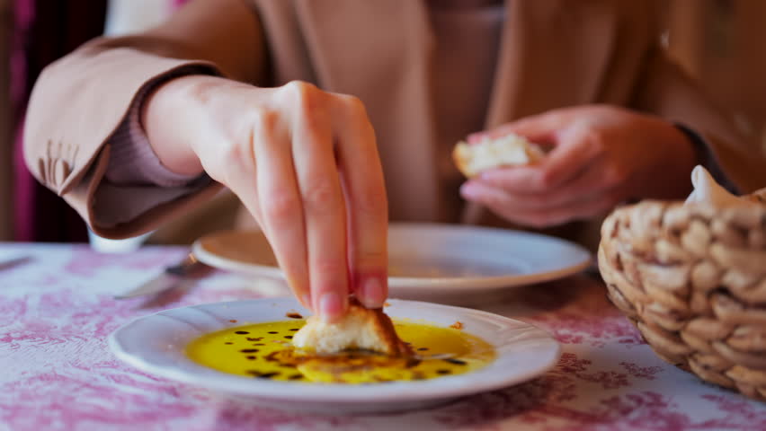Close up of a woman dipping bread in olive oil with balsamic glaze drops and eating it at a restaurant