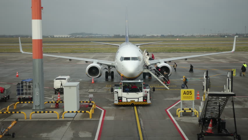 Plane with passengers, Mobile boarding, Airplane access. Using mobile staircase, passengers are boarding airplane on tarmac, with ground support staff and equipment present.