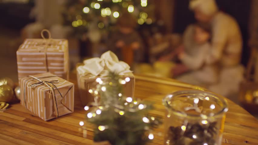 close up of christmas gifts on a table, grandmother playing with her grandchildren on the background stock video