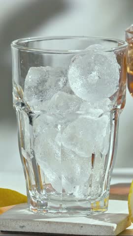 fresh  iced tea flowing in glass with ice  from glass carafe on sunny white wooden table top in slow motion