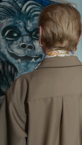 Vertical slowmo of elegant middle-aged Caucasian woman observing abstraction paintings on walls admiring artwork in modern art gallery