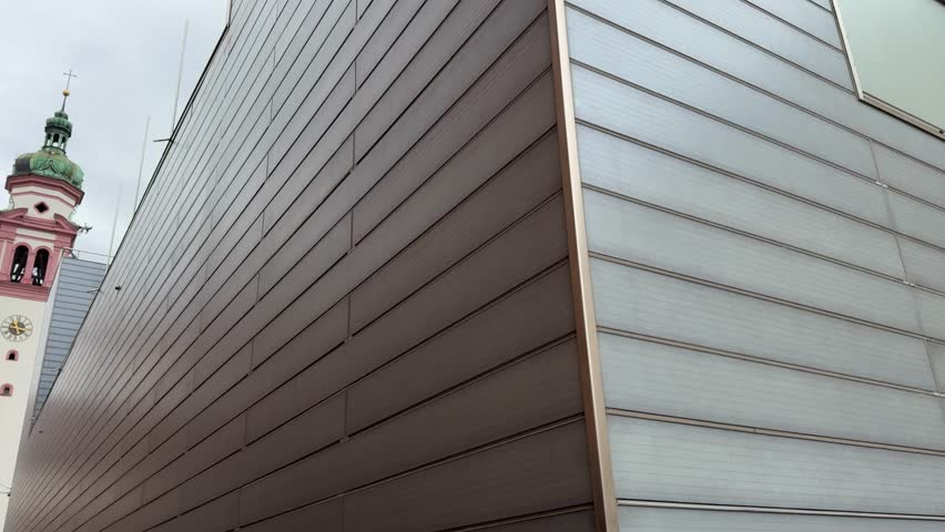 contrasting architecture featuring a historic church tower beside modern building facades against an overcast sky captures the mix of traditional and contemporary styles. Innsbruck Austria