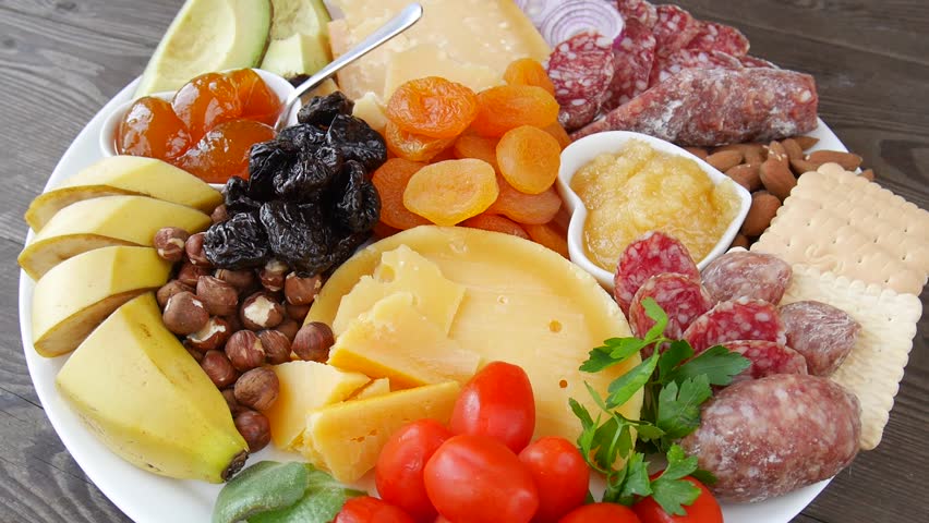 White ceramic platter with handcrafted cheeses, fresh fruit, dried apricots, nuts, crackers, and heart-shaped bowls of honey and apricot jam.