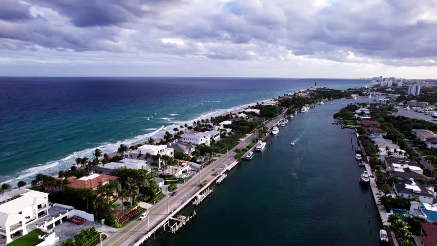 Boca Raton, Florida. Drone orbits around the Atlantic Ocean and Intracoastal Waterway. Boats, yachts, and luxury homes extend to the horizon. Golden hour.