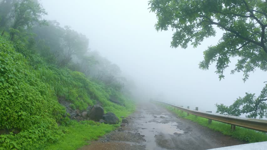 4K POV shot of a vehicle moving on a muddy road covered by fog in the middle of the forest in Sahyadri hills during the monsoon season at Maharashtra, India. Vehicle driving during foggy weather.