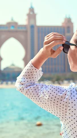 Happy woman in Dubai, vertical video with carefree brunette lady admiring architectural landmarks, back view. Summer vacation and holidays, traveling and relax, luxury rest in in UAE, slow motion
