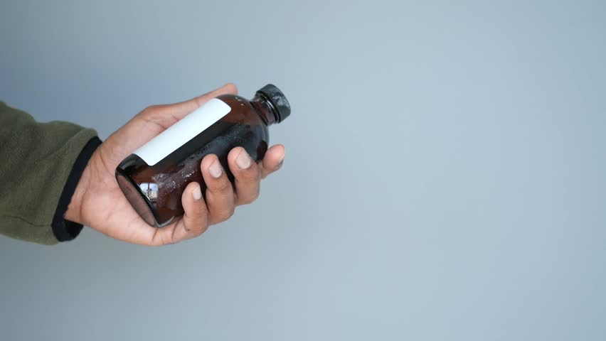 Holding a small glass bottle with a blank label in a neutral setting