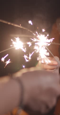 Vertical Screen : Young asia couple having fun and celebrates with sparklers lights in camping on beach at night. Male female traveler relax at campsite. Outdoor activity, adventure travel vacation.