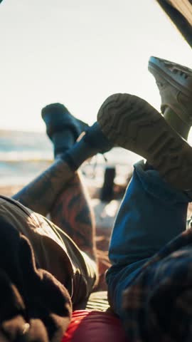 Carefree tourists resting in camp on sea shore, closeup view of legs, view from tent. Bright sunshine above water surface, local tourism and backpacking in nature, be calm and happy, two travelers