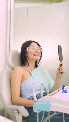 Hispanic woman looking in mirror after teeth whitening in dental office