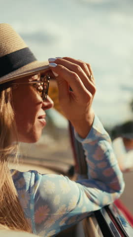 Beautiful blonde woman in luxury retro cabriolet, side portrait in sunny summer day. Vertical shot with attractive lady admiring architecture of city, enjoy luxury life, move on road by automobile