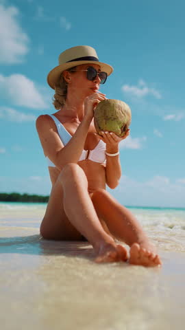 Summer vacation in paradise, woman sitting on shallow and drinking cocktail from coconut. Relax time in tropical island, recovery vitality and life energy, tanning and sunbathing on sandy beach