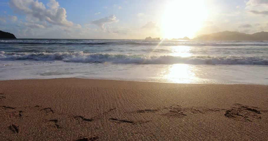 Beautiful sunset in sandy beach with waves. Footprints on sandy beach at evening. Evening waves on a beach in East Java.