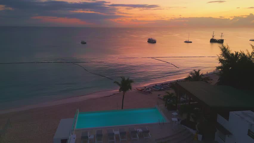 Stunning Sunrise in Punta Cana, Dominican Republic. Aerial View of Turquoise Pool, Sunbeds, Palm Trees Silhouettes, Yachts, and Sandy Beach. Vibrant Tropical Colors. Whala Bavaro. 2025