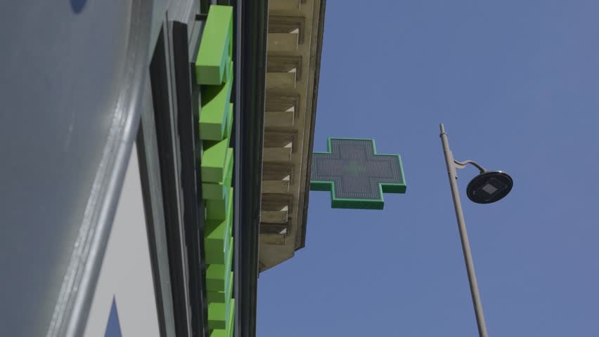 Green pharmacy cross sign against a bright sky in Paris, France, capturing the vibrant atmosphere