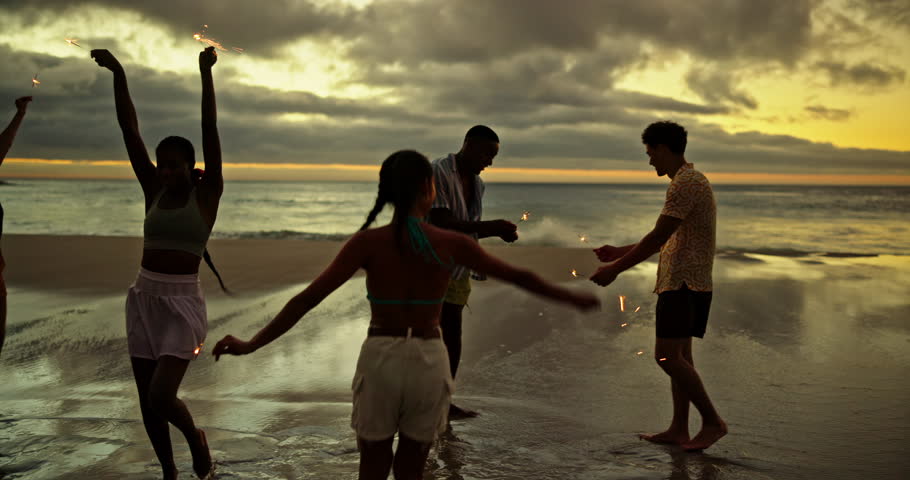 Happy, friends and dancing with sparkler on beach for ocean party, travel reunion and bonding together. People, fireworks and rhythm movement, New years celebration and sea sunset on freedom vacation
