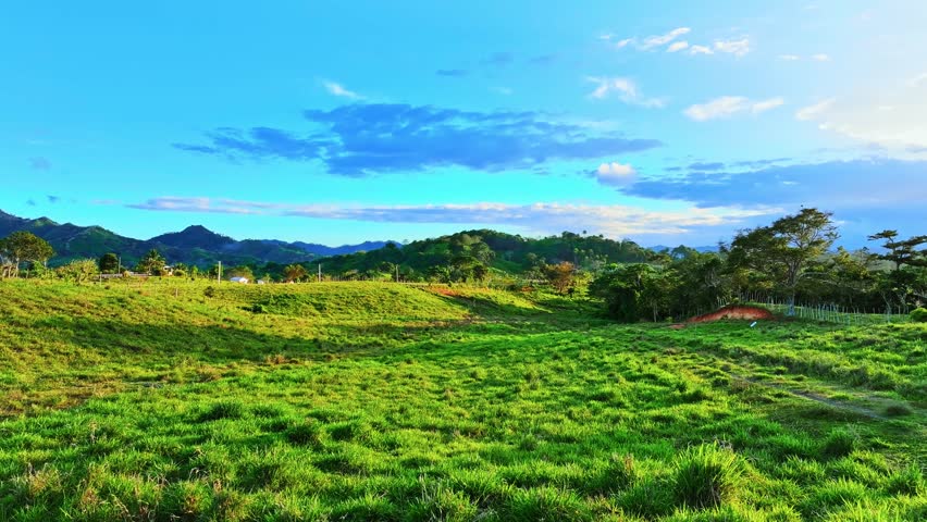 Summer mountain landscape in Dominican Republic. Drone view of green fields and meadows in summer. Mountain range against blue sky with white clouds. Wildlife landscape of America.