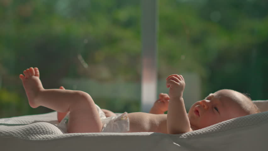 A newborn baby rests in a baby cocoon near an open sunlit window, absorbing natural sunlight for a healthy dose of vitamin D.