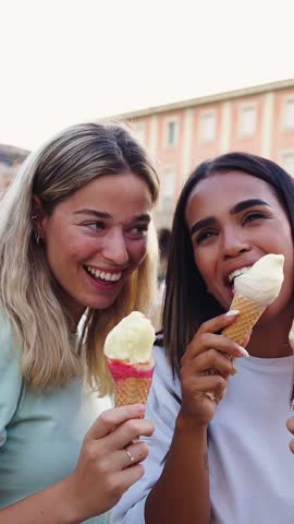 Vertical. Three young women enjoying ice cream cones, laughing and sharing joyful moments in a vibrant european city center during their summer holiday adventure