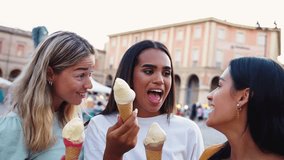 Three young women enjoying ice cream cones, laughing and sharing joyful moments in a vibrant european city center during their summer holiday adventure - Powered by Shutterstock - Get 15% off with code: PIKWIZARD15