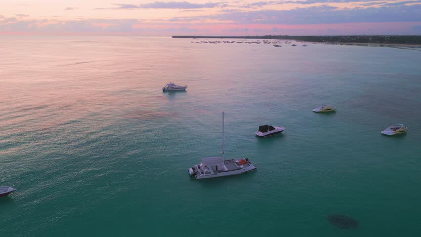 Aerial View of Catamarans and Boats Docked at Punta Cana Shoreline, Dominican Republic. Stunning Pink Sunrise Over Calm Turquoise Ocean Waters. Drone Footage. 2025