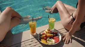 On this sunny day, two women enjoy poolside with colorful cocktails and a platter of fresh exotic fruits - Powered by Shutterstock - Get 15% off with code: PIKWIZARD15
