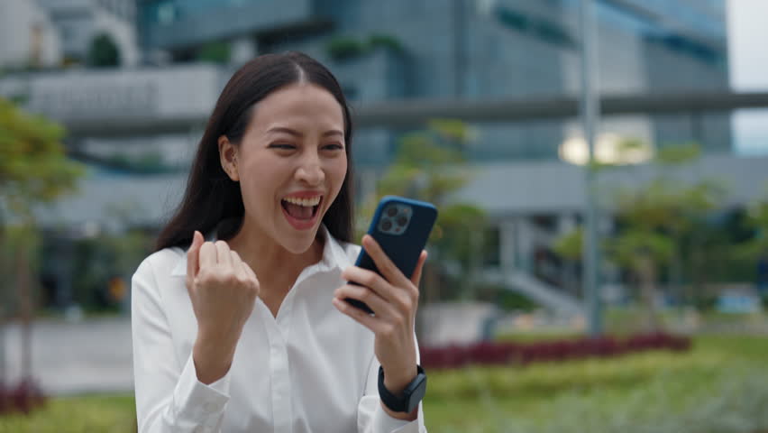 Happy Excited Woman Winning the Prize Online Using the Telephone. Happy Young Female Winner Outside Looking at the Screen and Shocked Screaming. People and Emotions Concept