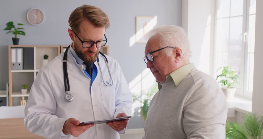 Elderly male patient consulting with a doctor or nurse using a tablet pc during a hospital or clinic visit. Modern healthcare, medical care, and digital online communication in medicine.