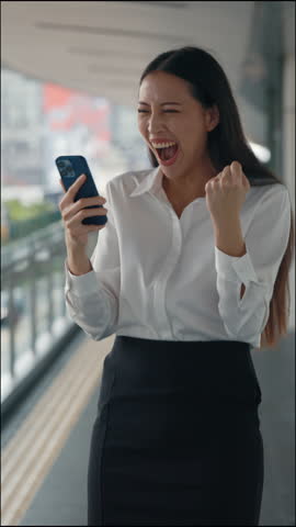 Vertical Video. Excited Charming Lady Using Telephone And Looking At Screen with Yes Gesture. Cute Attractive Business Woman Celebrates Good News Reading from The Smartphone. People And Victory