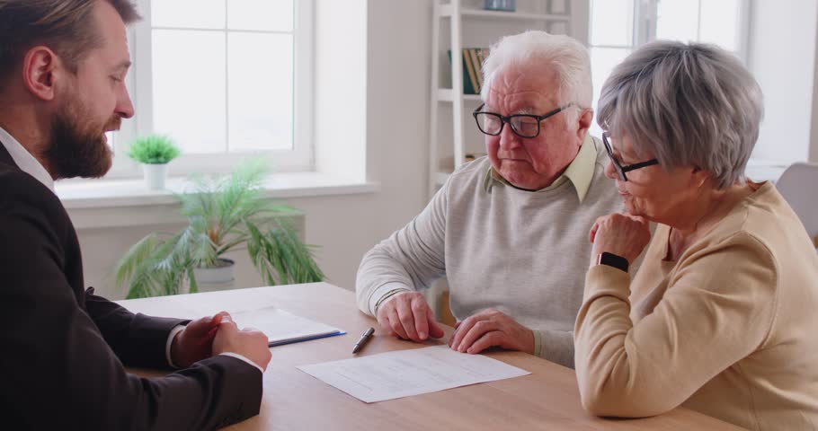 Real estate agent giving help to senior couple in buying new house, explaining terms of contract, purchasing property, sign papers. Elderly woman and man discussing financial matters 
