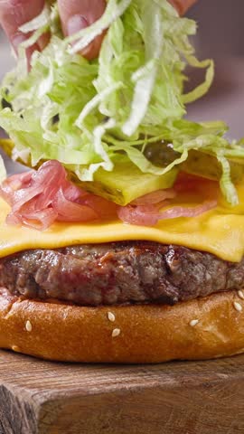 Chef preparing a juicy delicious beef burger in the home kitchen on a wooden board, food closeup