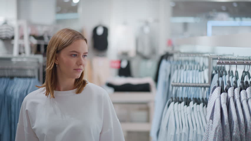 Woman walking through clothing store looking around at racks of stylish apparel, bright and organized setting features trendy fashion items
