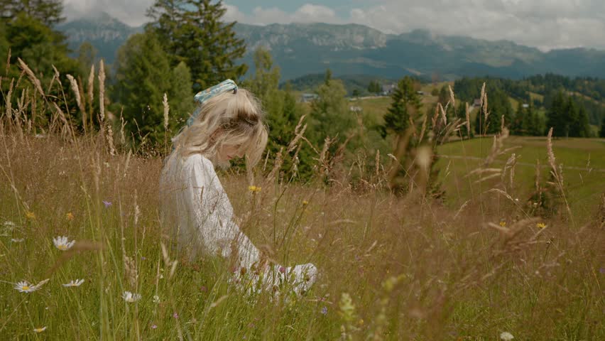 Pregnant woman sitting peacefully in wildflower meadow, gently caressing growing belly while absorbing serene mountain landscape during summer day