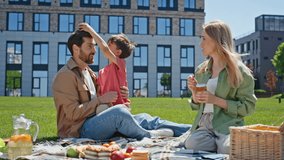 Joyful parents spending time with child boy in park. Happy family having fun eating together. Small kid playing with father at blanket. Man and woman talking at picnic preparing tasty lunch outdoors  - Powered by Shutterstock - Get 15% off with code: PIKWIZARD15