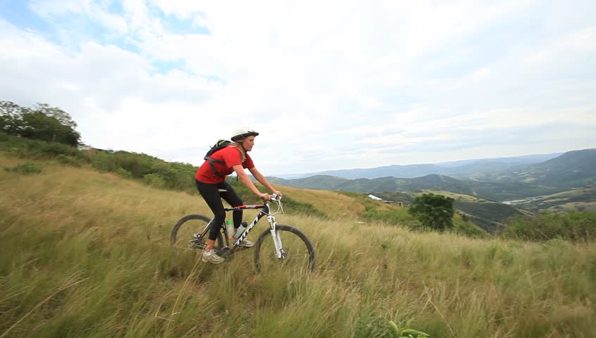 A pan shot of a girl riding on a pathway in between long grass .