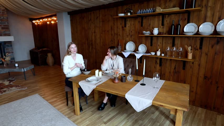Two friends enjoy a cozy meal together in a rustic dining space with elegant table setting