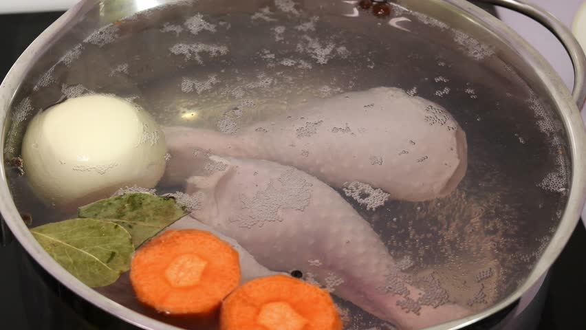 Chicken drumsticks, vegetables, bay leaves and peppercorns boil vigorously in bubbling water, creating rich homemade broth on stovetop.