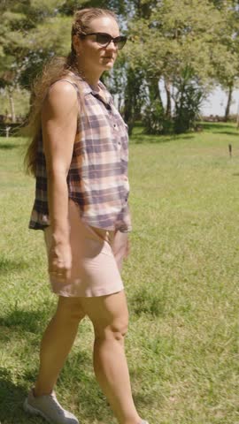Vertical video. Woman twirls joyfully on a Grassy Lawn under a Clear Sky, her arms outstretched, embracing the sunlight.