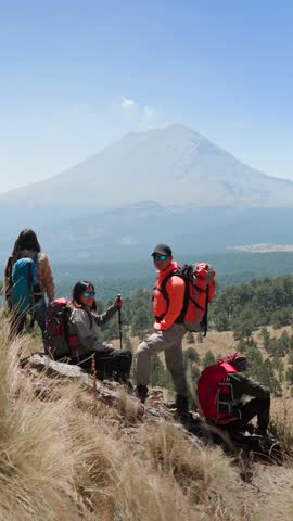 Four hikers are resting on a rock, enjoying the breathtaking view of popocatepetl volcano in mexico