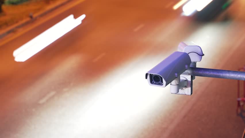 Surveillance enforcement camera monitor city traffic and speed control watching cars driving in the background. Timelapse long exposure effect