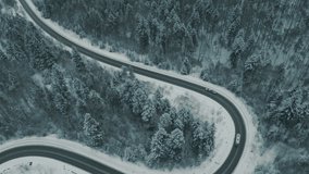 Aerial view of a winding snowy mountain road cutting through a dense winter forest. An SUV with a camper trailer slowly navigates the icy path, showcasing adventure, isolation, and serene nature. - Powered by Shutterstock - Get 15% off with code: PIKWIZARD15