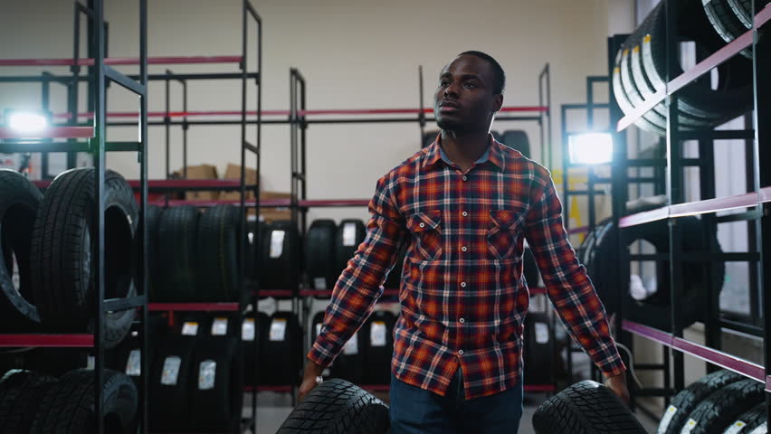 African American man carrying two tires in an auto parts store