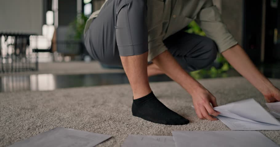 Close-up of a man in business attire quickly picking up paper sheets that fell onto the gray carpet ,while working in a modern office environment
